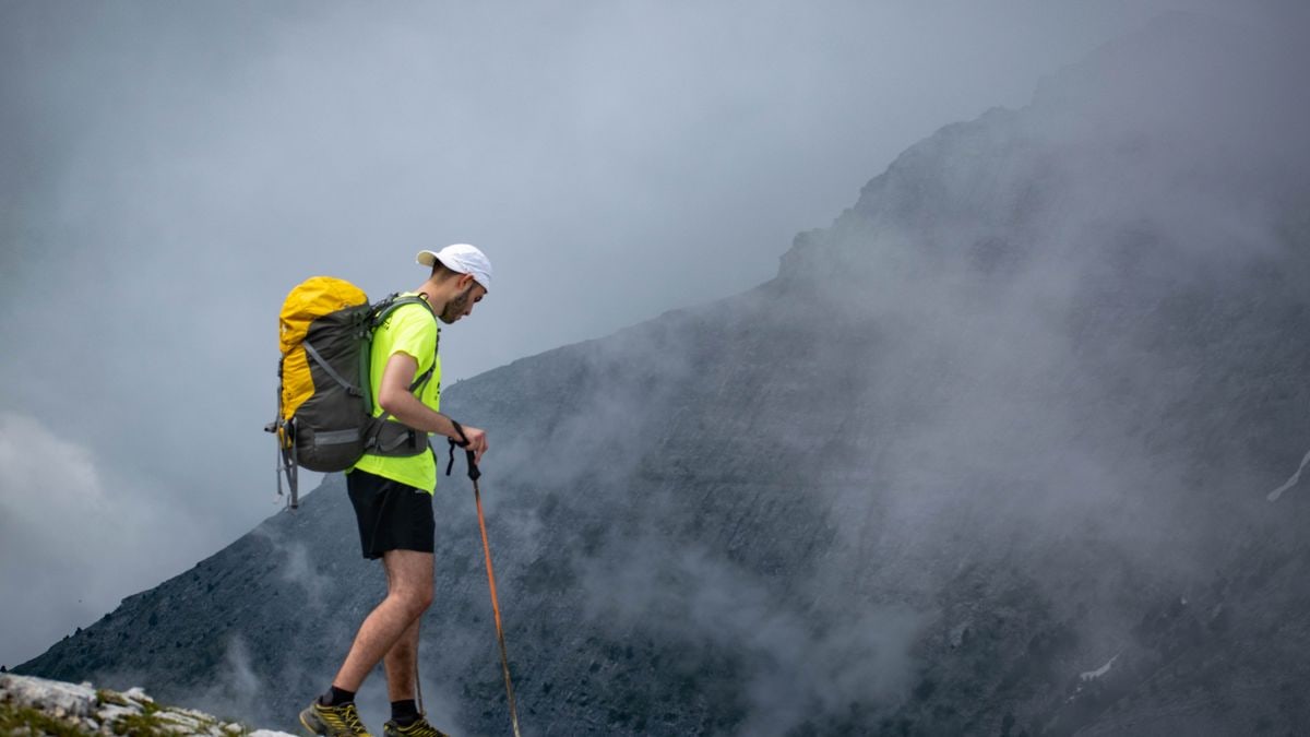 A lone hiker with a backpack explores the misty terrain of Olympos, Greece, capturing a sense of adventure.